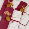Multiple burgundy wedding cards with wax seals arranged on white fur